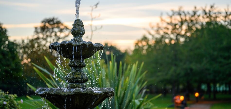 Fountain,with,water,drops,in,a,park,with,trees,behind